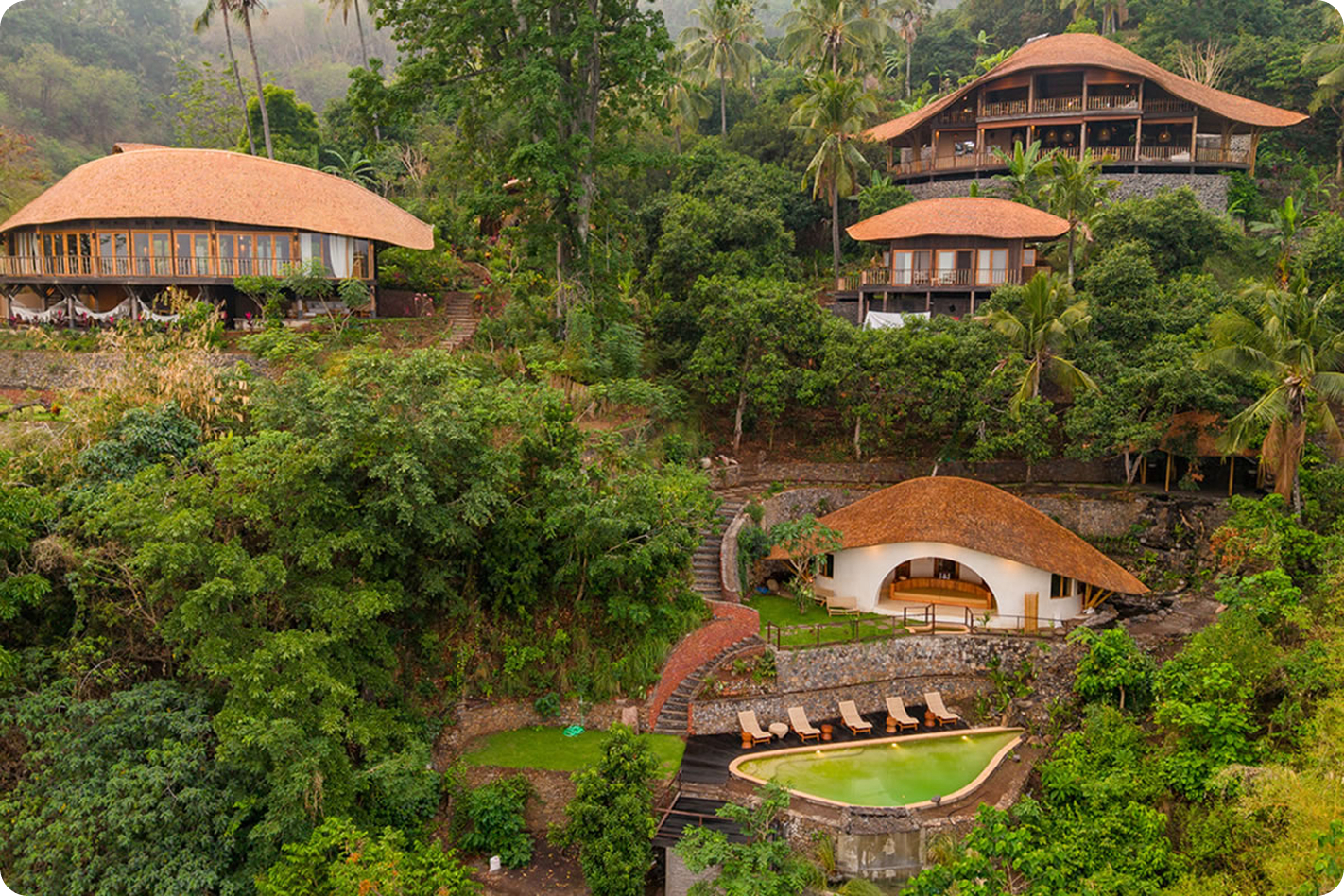 Aerial view of Bumi Cinta's thatched-roof buildings and infinity pool nestled into the jungle hillside