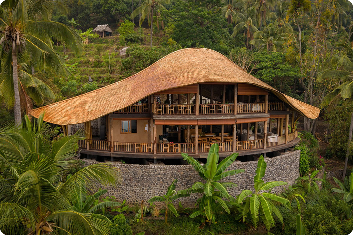 Wave-roofed communal hall with a curved thatched roof set on a stone foundation