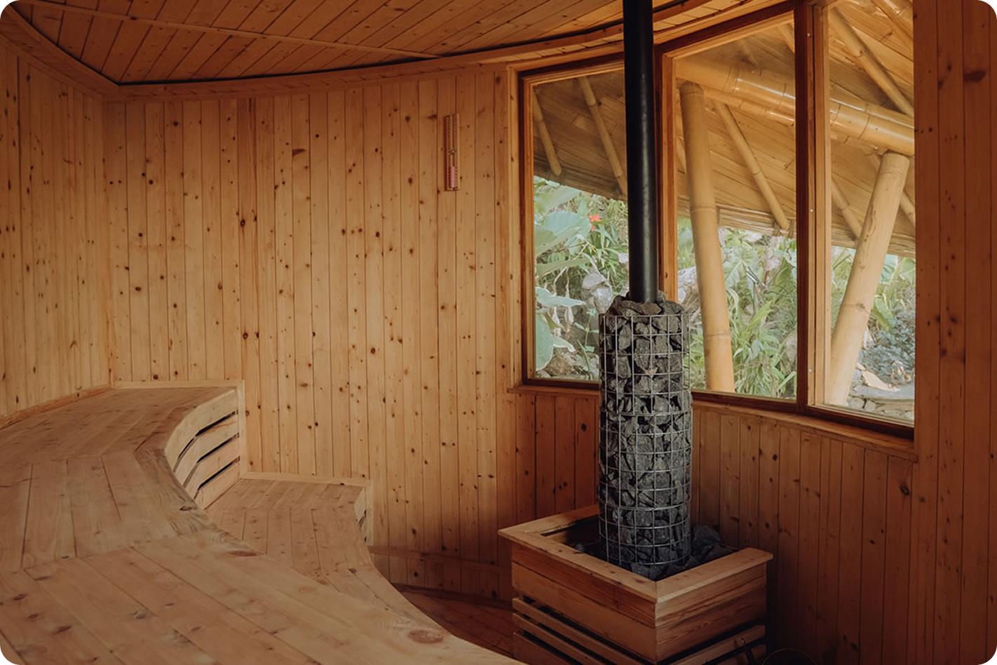 Wood-paneled sauna interior with a wood-burning stove and forest view